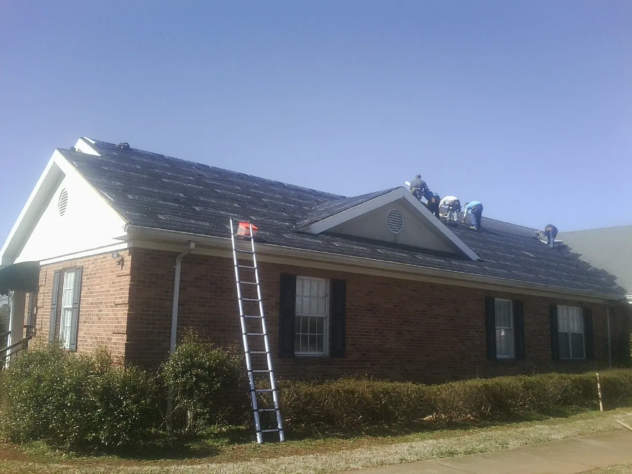 Crew tearing shingles off a brick ranch roof with a ladder set — Metal Roof Repair work by our crew in Cartersville