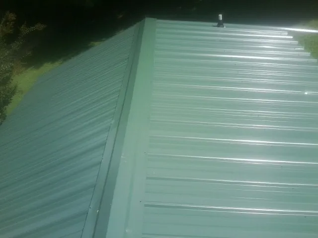 New green metal panels meeting at the ridge of a roof — Flat Roof Repair work by our crew in Cartersville